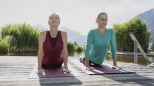 Zwei Frauen machen Yoga im Freien auf Matten.