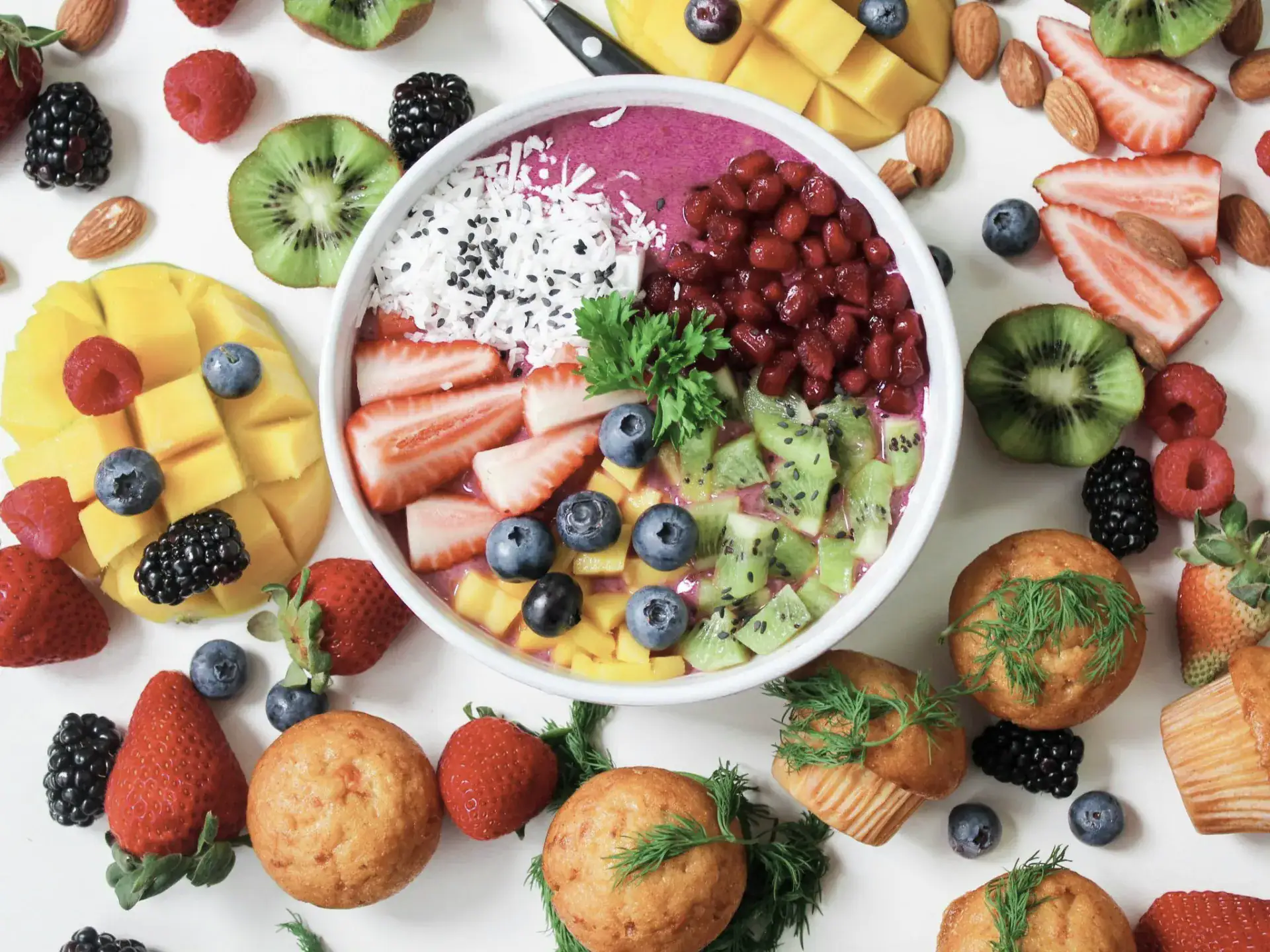 Regenbogen-Smoothie-Bowl mit frischem Obst und Muffins.